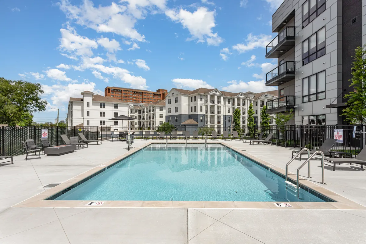 A modern resort-style apartment pool surrounded by lounge chairs, with sleek apartment buildings in the background. The scene is relaxed and inviting, suggesting a comfortable home base after a day out in the city.