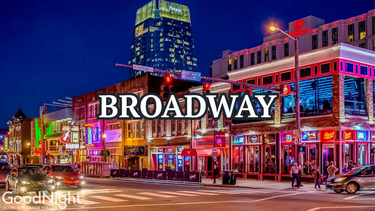A bustling Midtown Nashville street scene illuminated by vibrant neon signs, with crowds of pedestrians, cars passing by, and busy storefronts. Brightly lit buildings signal the area’s lively atmosphere of nightlife, live music, and dining.
