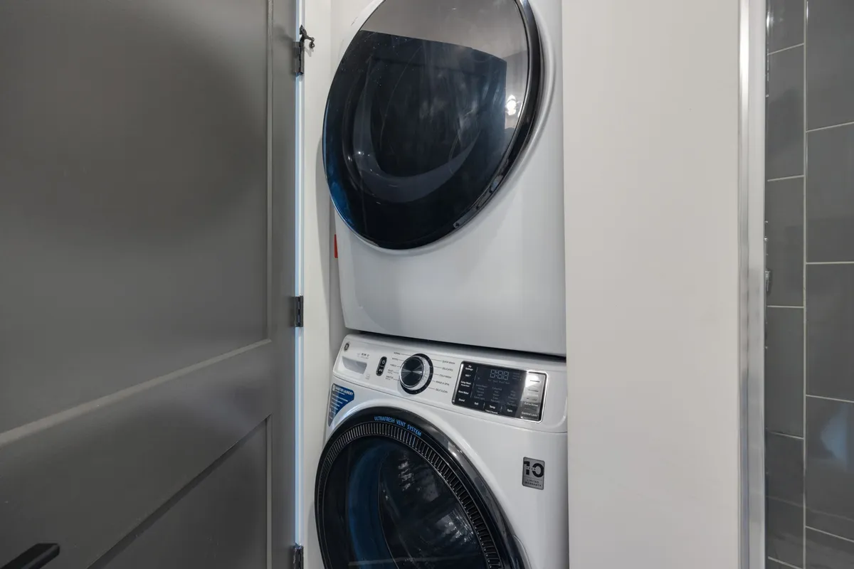 A compact laundry area featuring a stacked washer and dryer next to a doorway. The design is practical and modern, emphasizing in-unit convenience for guests and longer stays.