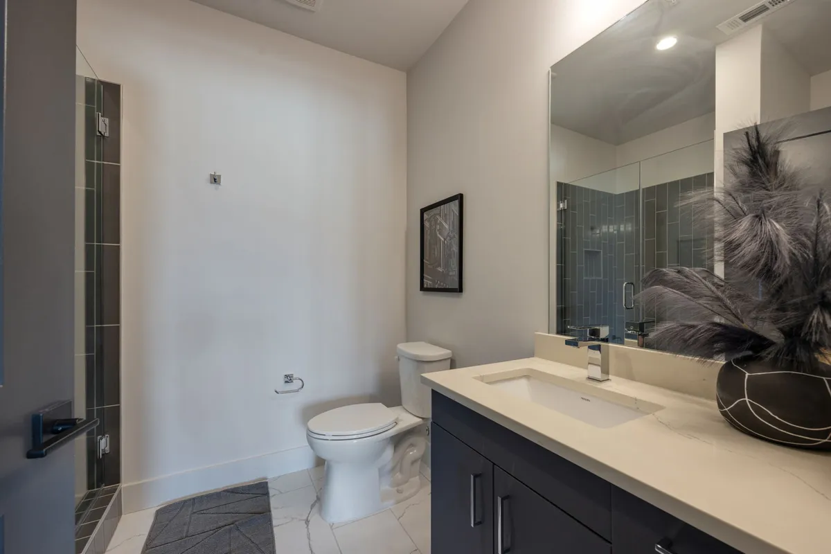 A serene, modern bathroom with a vanity sink, glass-enclosed shower, framed artwork, and a decorative plant. The space feels calm and refreshing, suited for self-care routines and relaxation after a busy day.