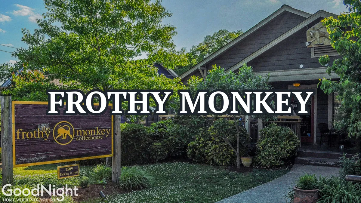 The exterior view of Frothy Monkey, showing its welcoming entrance and lush greenery. The signage is clear and inviting, establishing it as a popular local coffeehouse. The overall mood is friendly and vibrant, with an emphasis on the outdoor seating area that encourages socializing and relaxing.