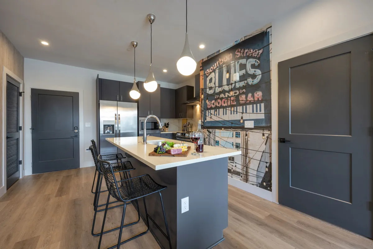 A lively kitchen scene with a central island countertop, stylish hanging pendant lights, bar stools for casual seating, and a decorative wall mural. The space is well-lit and designed for both cooking and socializing.