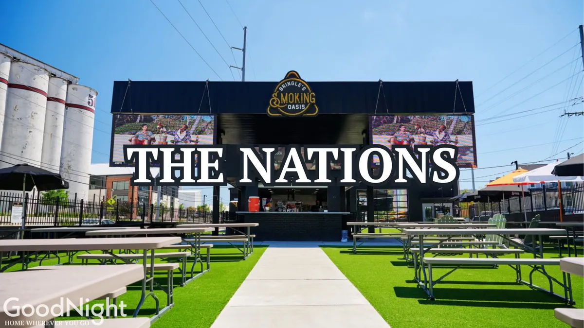 An inviting exterior scene featuring a large sign reading 'THE NATIONS', outdoor seating, and a food service counter, hinting at communal and social spaces where residents and guests can enjoy casual gatherings and events outside.