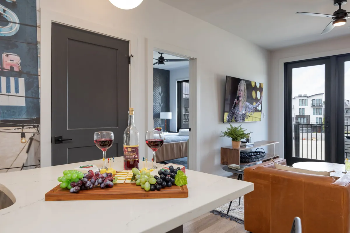 A modern living space set for entertaining, with a charcuterie board, wine, and a television displaying a live performance. The furniture is stylish and comfortable, suggesting a lively yet relaxed atmosphere ideal for catching up with friends or enjoying an evening indoors.