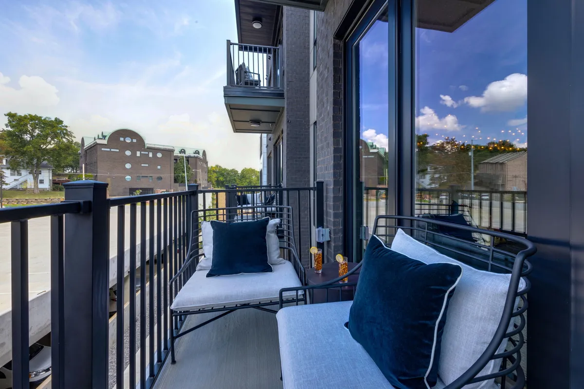 A serene private balcony featuring two cushioned chairs and a small table, framed by a balcony railing. The scene exudes tranquility, perfect for morning coffee or an evening drink while enjoying neighborhood views.